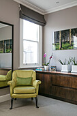 Lime green armchair and mirror with sideboard at window in London home UK