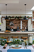 Schwarze Pendelleuchten über der Frühstücksbar mit einem für das Weihnachtsessen gedeckten Tisch in einem Haus im Stil der 1930er Jahre in West Sussex, Großbritannien