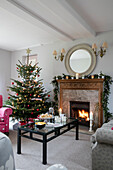 Schwarzer Couchtisch und beleuchtetes Feuer mit Weihnachtsbaum in Arts and Crafts home West Sussex UK