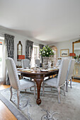 Silver candlesticks and lilies on vintage dining table with upholstered chairs in Wiltshire home England UK