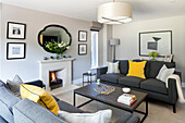 Zwei graue Sofas mit gelben Kissen und Kaminfeuer im Wohnzimmer eines Hauses in Surrey, Großbritannien
