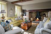 Yellow sofa and lamps with wooden chest at lit fireside in Somerset home UK