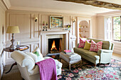 PInk blanket on armchair with light green sofa at lit fireside in Somerset home UK