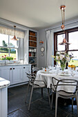 White cloth on circular table with grey chairs in Devon farmhouse kitchen UK