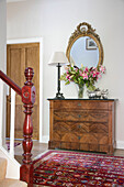 Cut lilies and gilt framed mirror on wooden chest of drawers in hallway of Hampshire home UK