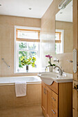 Cut flowers on windowsill of Hampshire bathroom with wooden wash stand and basin UK