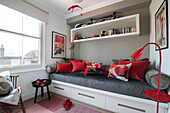Rote Kissen und Spielzeug auf Regalen über einem grauen Einzelbett in einem Haus im Norden Londons UK
