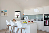 White bar stools at kitchen island with oven and light blue splashback in newbuild Cornwall UK