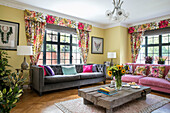 Pink and grey sofas with low wooden coffee table in modernised 1900s Arts and Crafts style London home UK