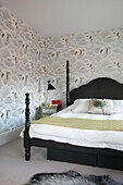 Schwarze Lampe und Doppelbett mit Storchenmustertapete in einem Londoner Haus UK