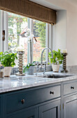Große silberne Kerzenständer und Kräuter an einem Marmorspülbecken im Fenster einer Küche in Oxfordshire UK