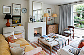 Velvet sofa with books on ottoman at lit fireside in London home UK