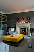 Yellow velvet ottoman at fireside with bookcase in Hampshire home UK