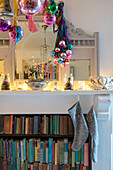 Christmas baubles with lit candles on fireplace with vintage book storage in Norwich home Norfolk UK