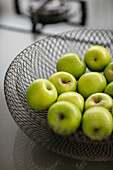 Wire mesh basket of bright green apples in London home UK