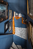 Framed pictures and gold fabric in blue staircase of Sussex home