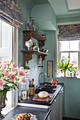 Lilies and tulips in kitchen with carved wooden shelves and roman blinds in Sussex home