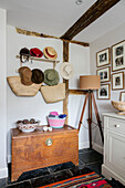 Hats and bags above wooden chest with tripod lamp in Hampshire home England UK