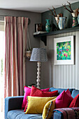 Grey sofa with bright cushions and striped curtains under shelf in Hampshire home England UK