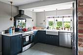 Gold pendant lights in kitchen with teal units and mirrored splashback Hampshire England UK