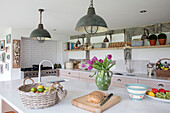 Industrial pendants above kitchen island with tulips and fruit basket in Surrey farmhouse UK