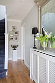 Grecian vase on pedestal with framed prints in hallway of Surrey cottage UK