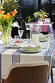 Vase of tulips on striped tablecloth with place setting and wooden chair in London home UK