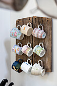Assorted cups hang on wooden board in Surrey cottage UK