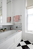 PInk towel on rail above bath with mirrored cabinets in London townhouse UK