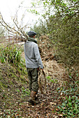 Mann trägt Zweige über der Schulter in Isle of Wight Waldgebiet UK