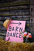 Sign for BARN DANCE on haybale outside rustic wood cabin in Autumn UK