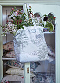 Cotton bag filled with fresh flowers hanging on a glass cabinet door