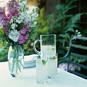 Kühle Getränke auf einem Gartentisch mit Blumenarrangement an einem Sommertag