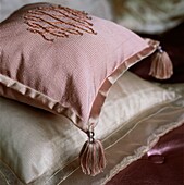 Rosa Kissen mit gestickten Verzierungen und Quasten auf einem Bett