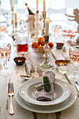 Festive table setting in dining room with lit candles and place set with plat bowl and napkin tied with a bell and pine twig