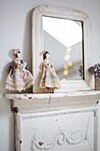 Detail von Vintage-Puppen auf weiß gestrichenem Kaminsims mit Spiegel, in dem sich das Dachfenster im Schlafzimmer im Dachgeschoss spiegelt