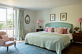Bed with throw pillows, antique bedside tables and pink armchair
