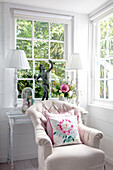 Light-coloured reading corner with armchair, floor lamps and flower arrangement