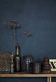 Dark blue wall, glass bottles and decorative objects on a wooden shelf