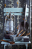 Old gardening tools and paraffin lamp on wooden chair in front of weathered wall