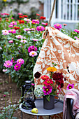 Gemütliche Gartenecke mit Blumen und Laterne auf Beistelltisch, gemustertes Tuch als Abtrennung