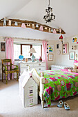 Wooden bed with colourful duvet and doll's house in rustic, child's bedroom