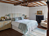 Doppelbett, Nachtschränckchen und Kamin im Schlafzimmer mit Kassettenvertäfelung und Holzbalkendecke