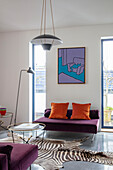 Violette Sitzmöbel, darüber abstrakte Kunst im Wohnzimmer, runder Coffeetable auf Zebrafell