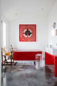 Rote Accessoires im Badezimmer mit weißen Wänden und Betonboden