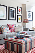 Ottoman with striped cover, sofa with throw pillows and a gallery wall with modern, abstract art collection