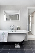 Freestanding bathtub with monogrammed towel and mirror in modern bathroom