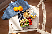 Lunchbox mit gefülltes Pitabrot, Granola, Tomaten und Blaubeeren auf einem Stuhl
