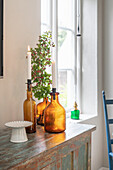 Candles in colored glass bottles on wooden table next to window