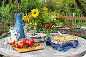 Garden table set in autumn with apples, sunflowers and apple crumble